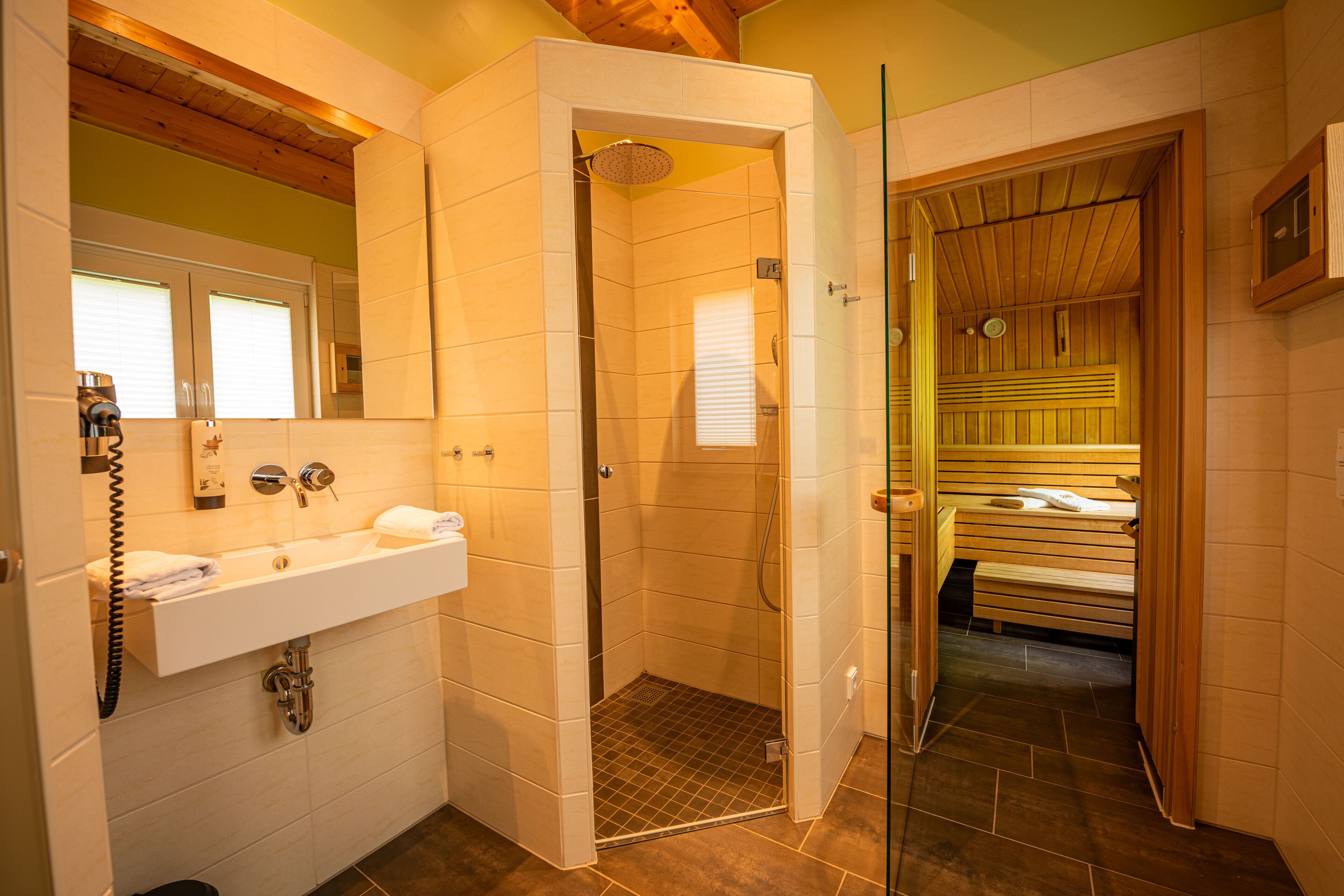 Een badkamer met een douche, wastafel en een houten sauna.