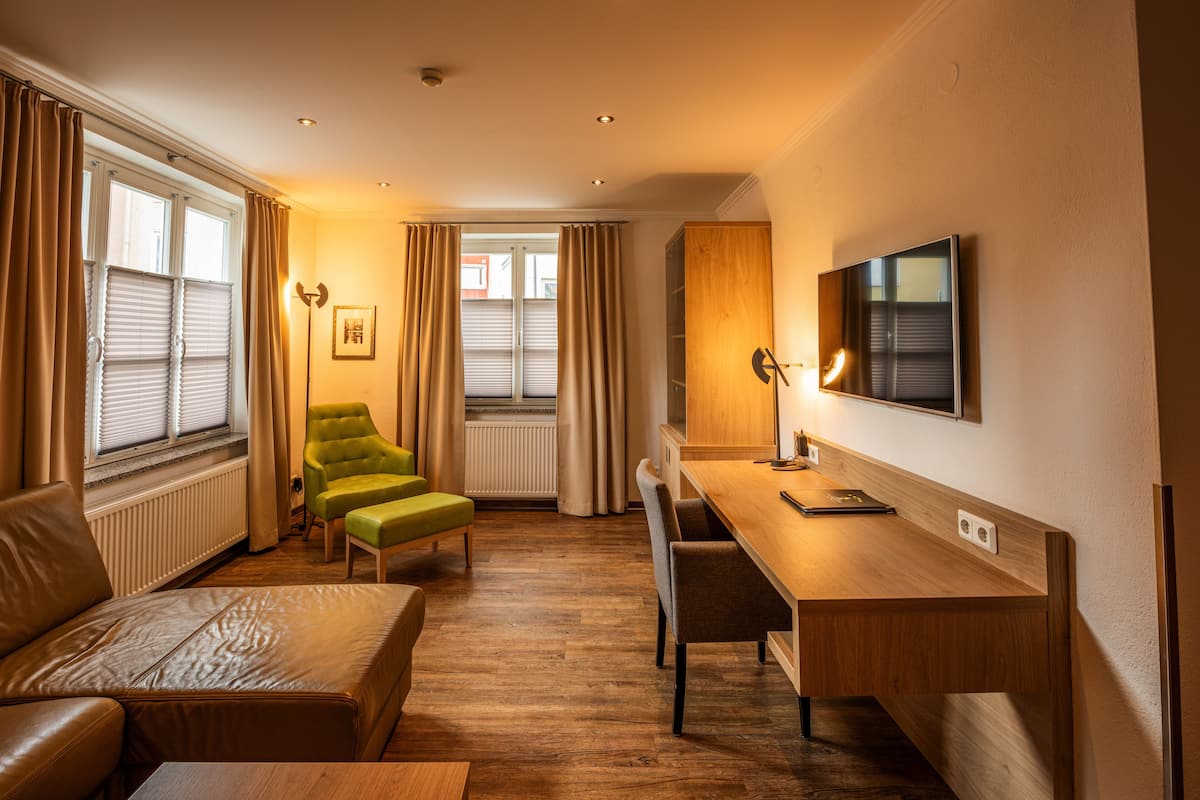 Een moderne hotelkamer met een houten bureau, een leren bank en twee fauteuils.
