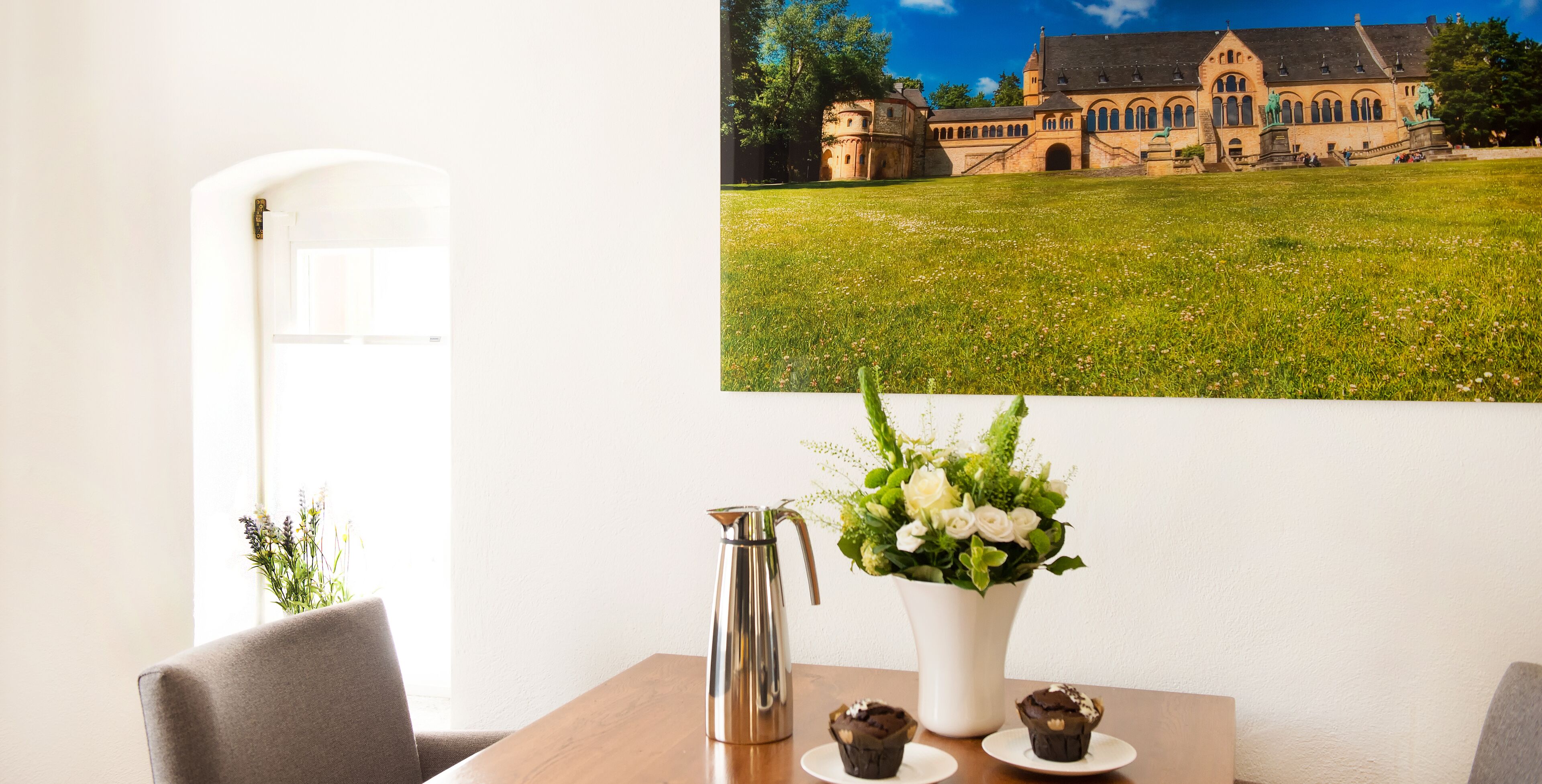 A dining area with a table, chairs, a vase with flowers, and a metal pitcher.