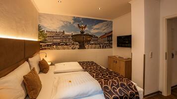 Een hotelkamer met een bed, een houten hoofdeinde, een muurschildering van een stadsplein en een klein kastje.