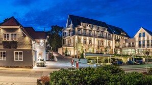Um hotel de vários andares com estilo arquitetônico europeu tradicional, apresentando um pátio central com área coberta por uma cúpula de vidro e vários níveis de estacionamento.