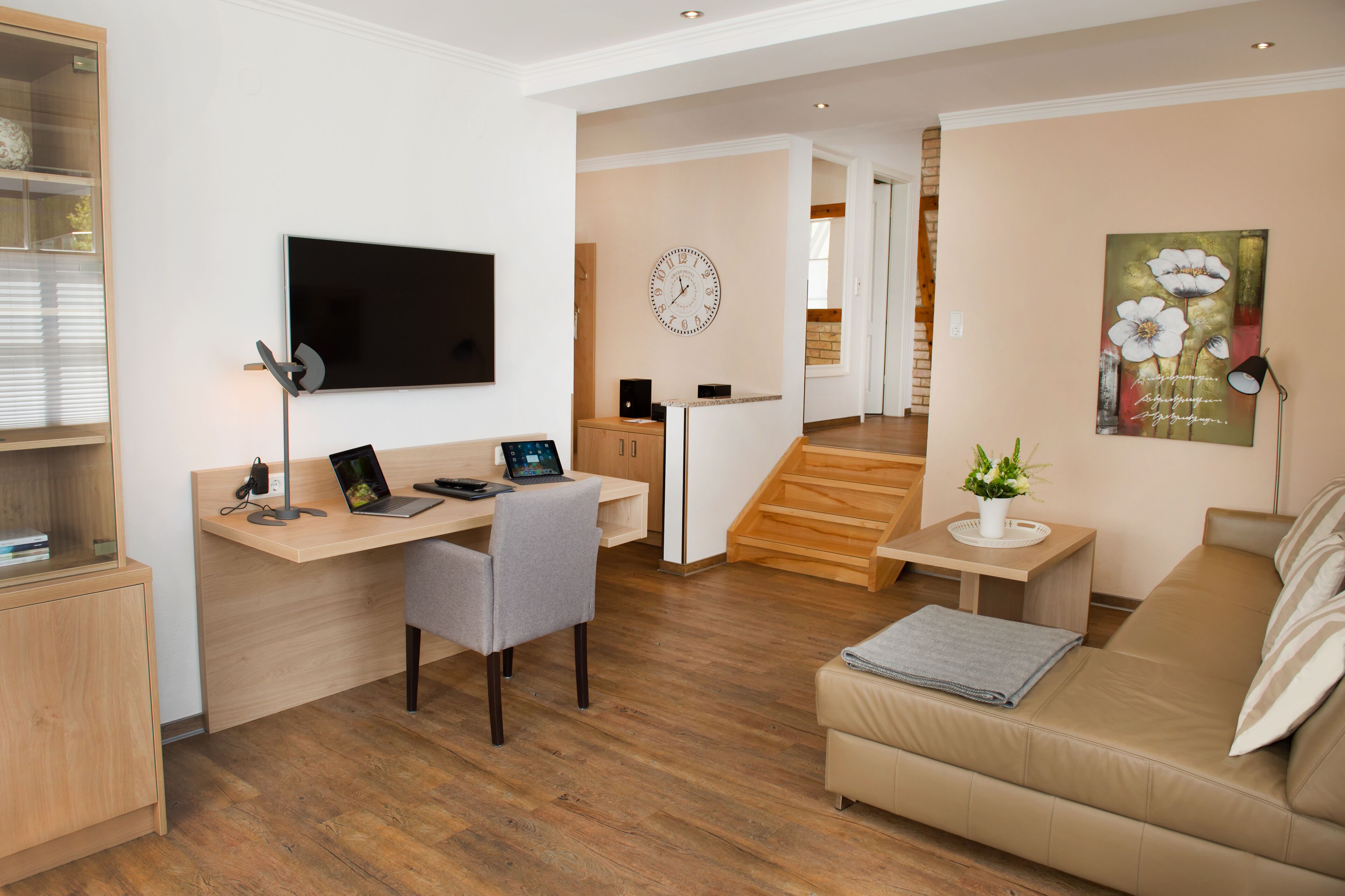 A modern living room with a wooden desk, a sofa, a TV, and a staircase leading to another room.