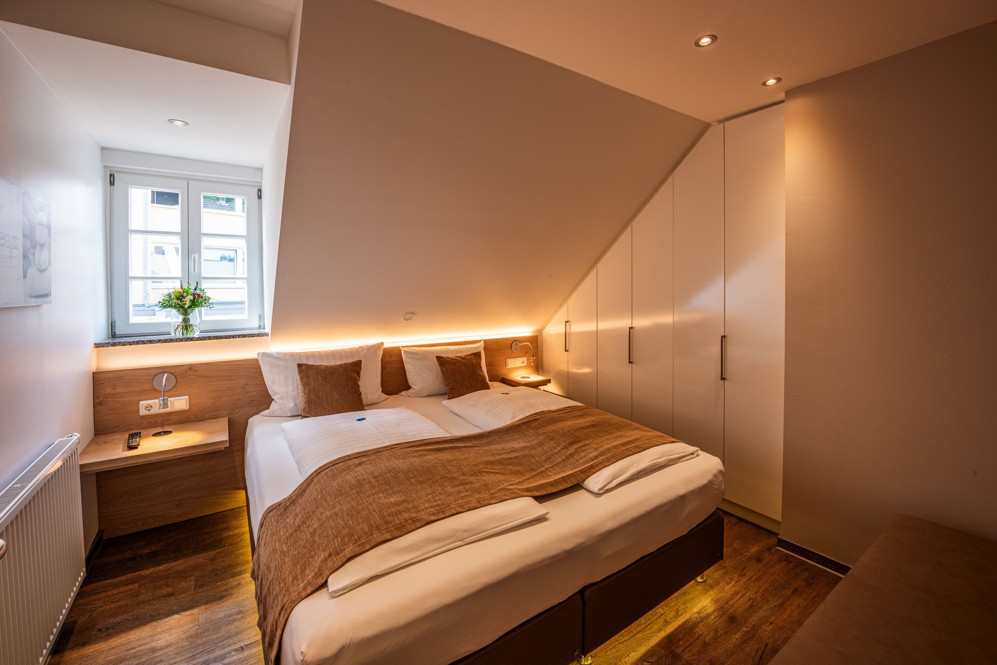 A modern bedroom with a large bed, bedside tables, a window with a view, and built-in wardrobes.