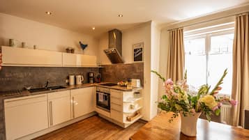A modern kitchen with white cabinets, a wooden countertop, and a built-in oven. There is a window with curtains and a vase of flowers on the counter.