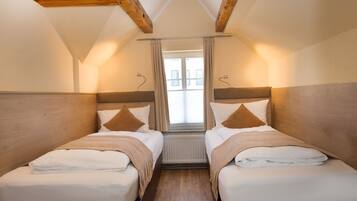 Ein Zimmer mit zwei Betten, Holz-Kopfteilen, einem Vorhangfenster und einem Heizkörper zwischen den Betten.
