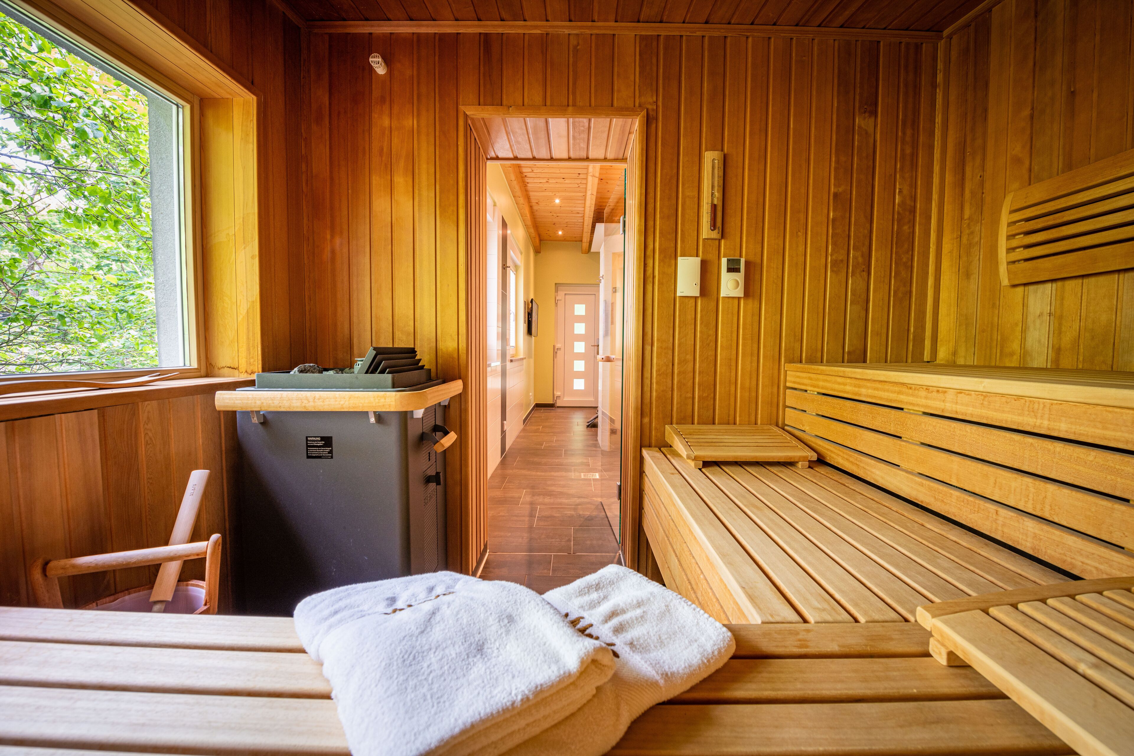 A sauna room with wooden benches and a bench with towels. There is a sauna heater and a small table with a towel on it.