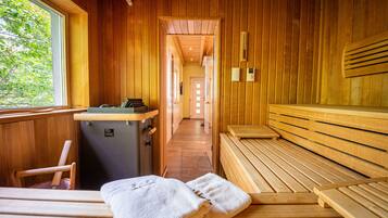 A sauna room with wooden benches and a bench with towels. There is a sauna heater and a small table with a towel on it.
