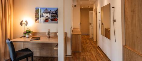 A modern hotel room with a wooden floor, a desk with a chair, a lamp, and a framed picture on the wall.