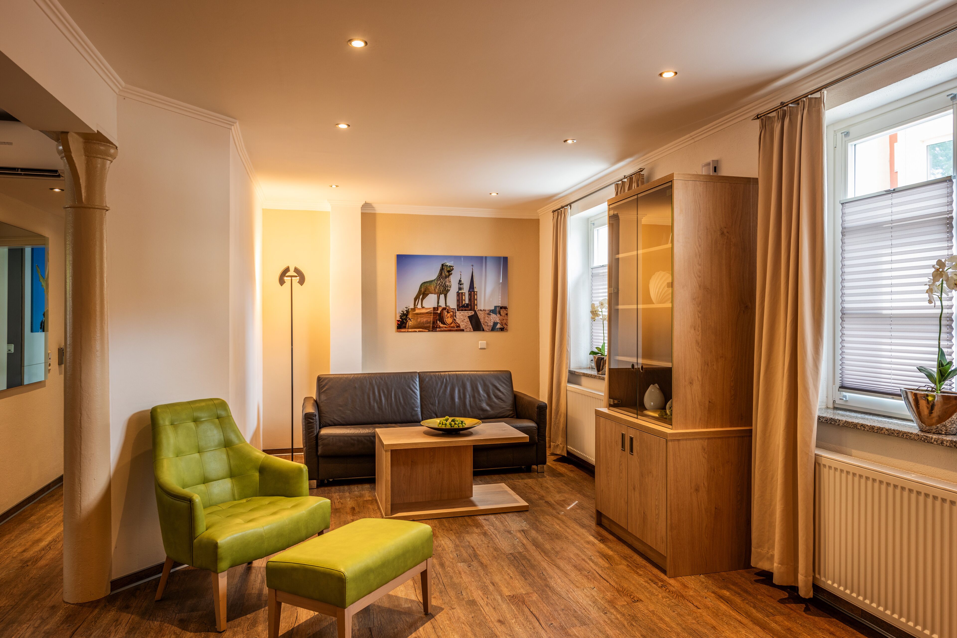 Ein modernes Wohnzimmer mit einem grünen Sessel, einem grauen Sofa, einer Holzkommode und einem Stadtbild.