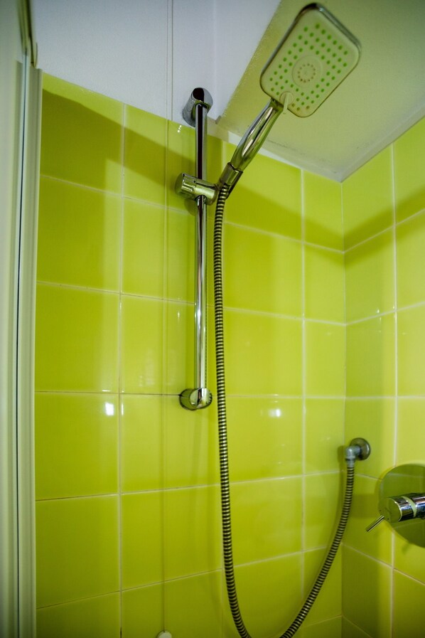 Une douche équipée d’un flexible chromé et d’une douchette à main fixée sur un mur recouvert de carreaux vert vif.