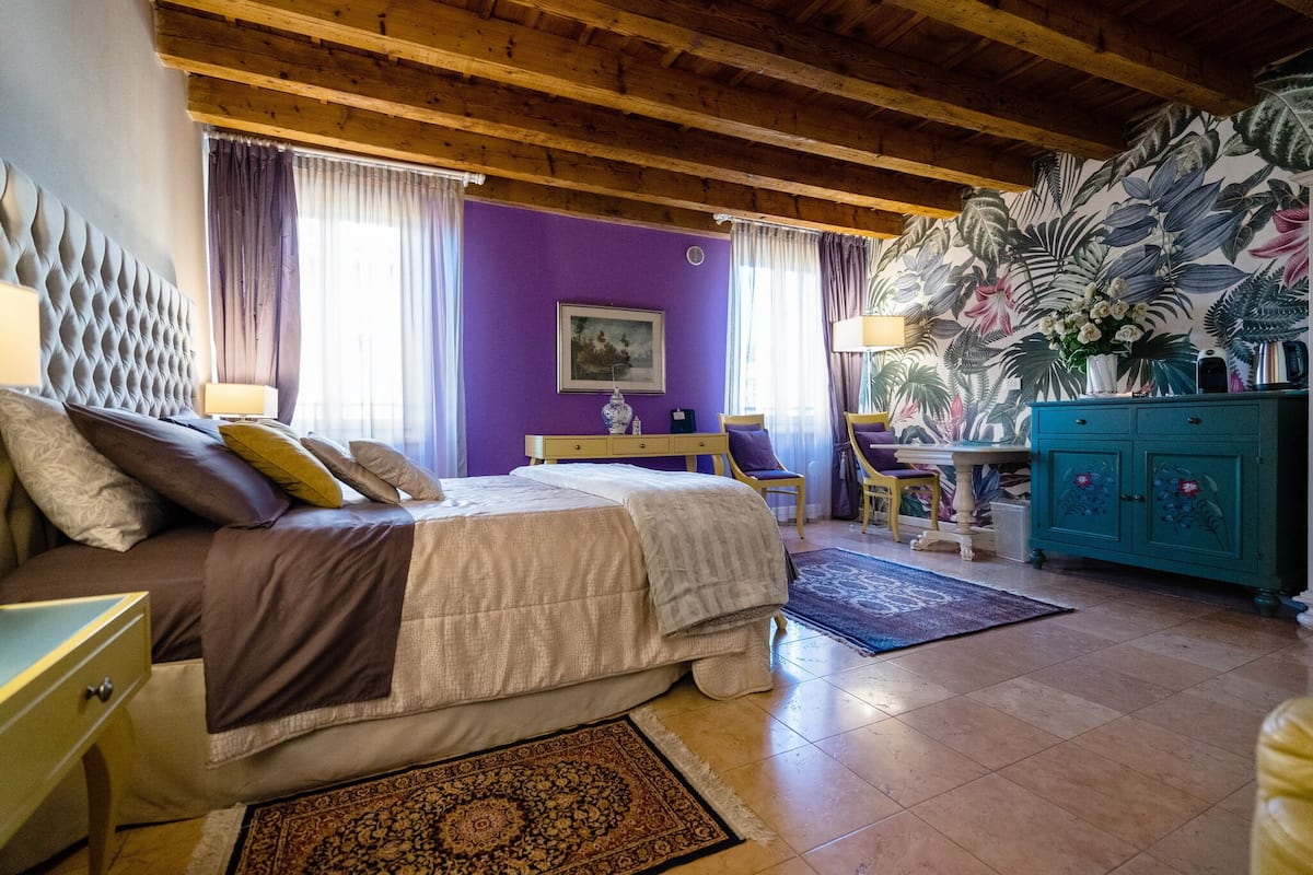 A bedroom with a bed, a desk, a chair, a cabinet, and a large floral wall mural.