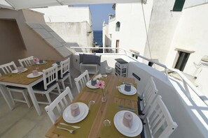 A dining area with white furniture, a table set for four, and a view of the sea through a narrow street. - B&B Fiore (Gallipoli)