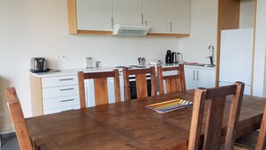 Ett kök med ett träbord och stolar, vita skåp och ett vitt kylskåp.