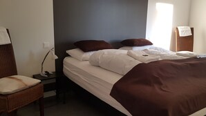 En snyggt bäddad säng med vita och bruna sängkläder, ett sängbord med en lampa och en stol med en kudde.