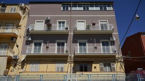 A multi-story building with balconies, air conditioning units, and a blue fence. - B&B Nodo Francescano (Porto Empedocle)