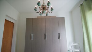 A room with a large wardrobe, a wooden door, a white chair, and a green curtain. - B&B Nodo Francescano (Porto Empedocle)