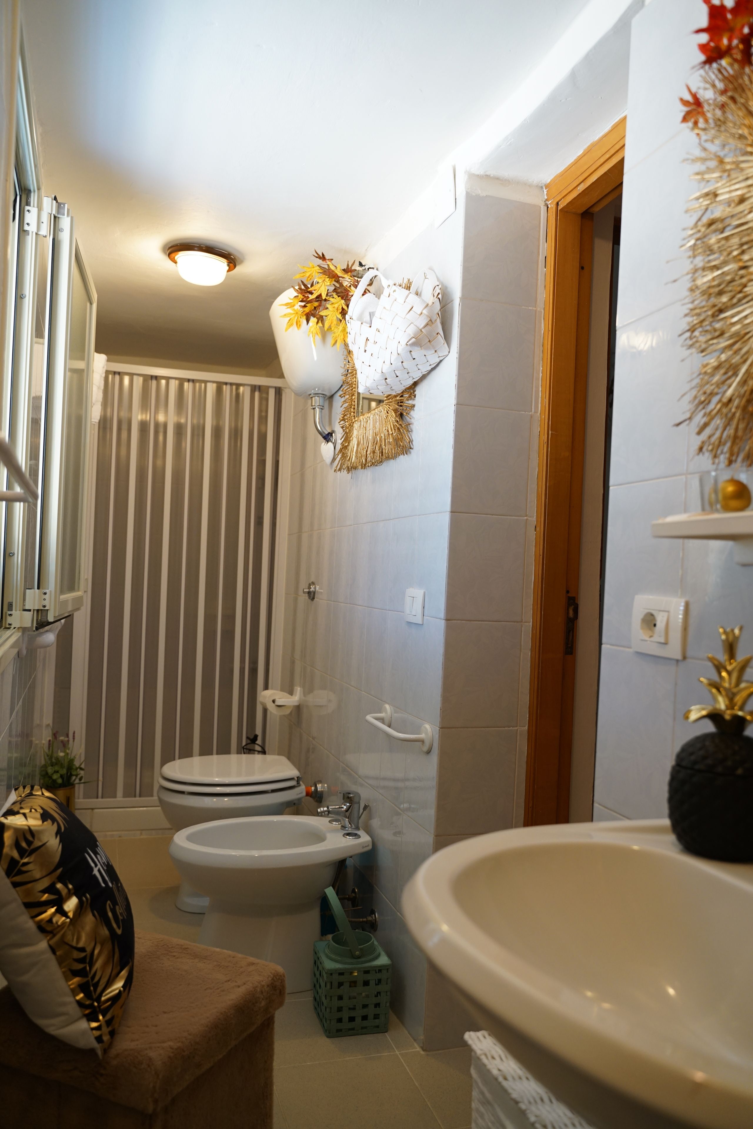 Un baño con inodoro, bidé y lavamanos. Hay plantas decorativas y un perchero para toallas.