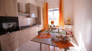 A modern kitchen with wooden cabinets, a gas stove, and a dining area with a table set for breakfast. - B&B Nodo Francescano (Porto Empedocle)