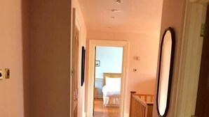 Un pasillo con suelo de madera que conduce a un dormitorio con cama y mesita de noche.