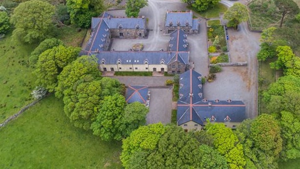 Vista aérea de una extensa propiedad con varias construcciones, incluyendo una casa principal con techo simétrico y otras edificaciones más pequeñas.