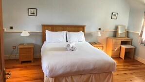 Una cama bien hecha con sábanas blancas y toallas enrolladas, cabecera de madera, mesitas de noche con lámparas y un pequeño escritorio con espejo.