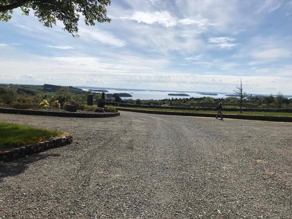 Un espace de stationnement recouvert de gravier offrant une vue sur une étendue d’eau et sur la terre ferme au loin.