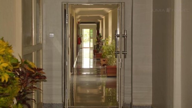 A long, narrow hallway with a reflective floor leading to a door at the end. There are potted plants along the sides and a clear view of the door's interior. - Bilton Continental Hotel (Owerri)