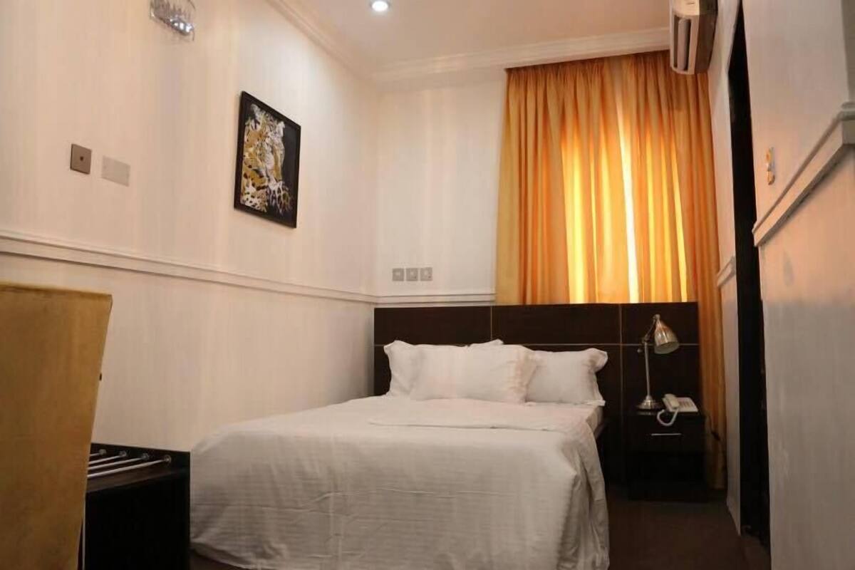 A hotel room with a bed, a nightstand with a lamp, a telephone, and a painting on the wall.