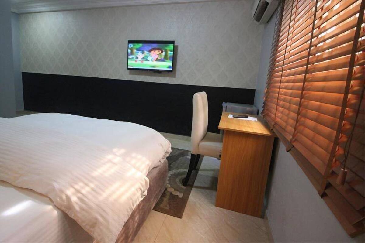 A hotel room with a bed, a desk, a chair, a television, and a window with blinds.