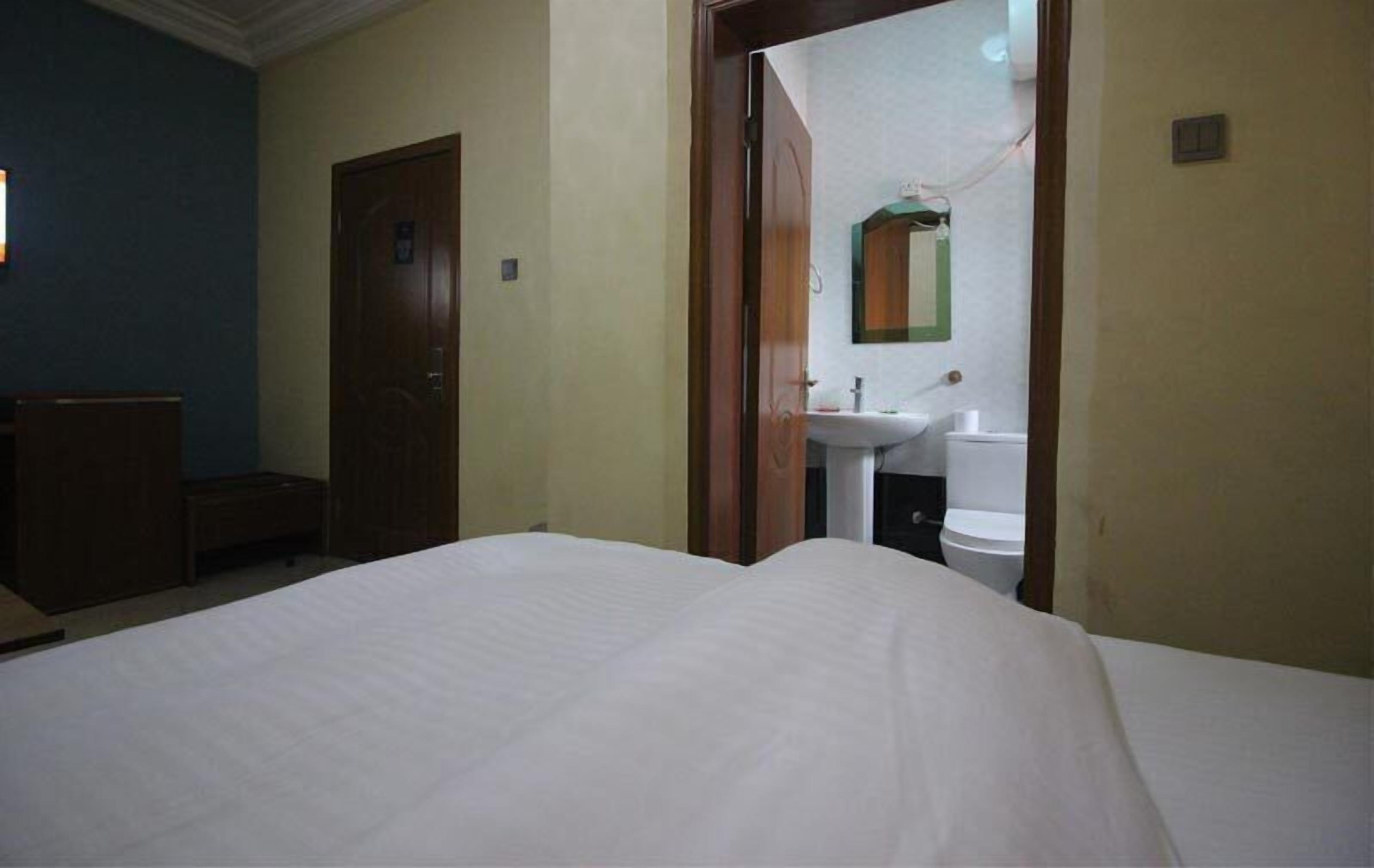 Une chambre d’hôtel avec un lit, une armoire en bois et une salle de bain visible à travers une porte ouverte.