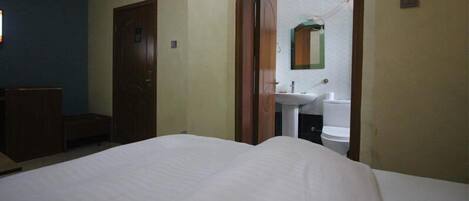 A hotel room with a bed, a wooden wardrobe, and a bathroom visible through an open door.