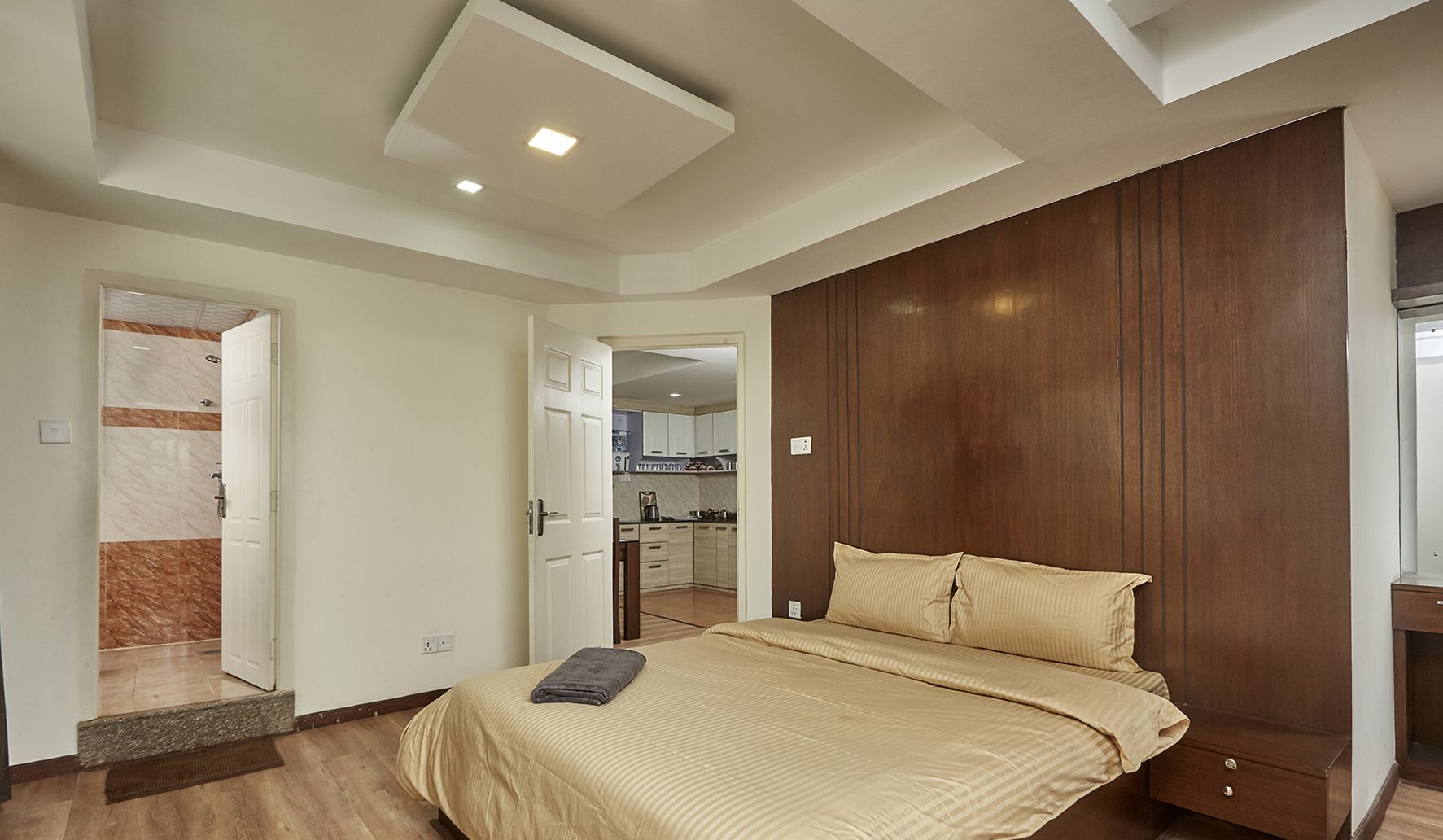 A bedroom with a bed, wooden wardrobe, and a view into the kitchen.