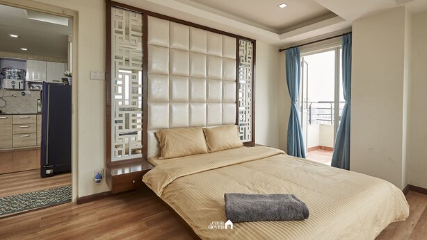 Une chambre à coucher avec un lit, un plancher en bois, une tête de lit intégrée, une fenêtre avec des rideaux et une vue sur l’extérieur.