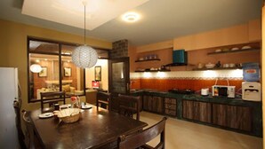 A dining area with a wooden table and chairs, a hanging light fixture, and a kitchen area with wooden cabinets and a countertop. - Kathmandu Heritage Home by Casa Deyra (Kathmandu)