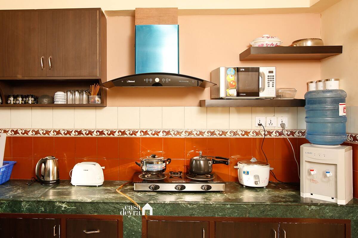 A kitchen with a stove, microwave, and various appliances. There are cabinets, a water dispenser, and a blue water bottle.