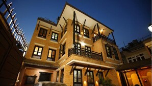 A multi-story building with a balcony on the second floor, a garage entrance, and a car parked in front. - Kathmandu Heritage Home by Casa Deyra (Kathmandu)