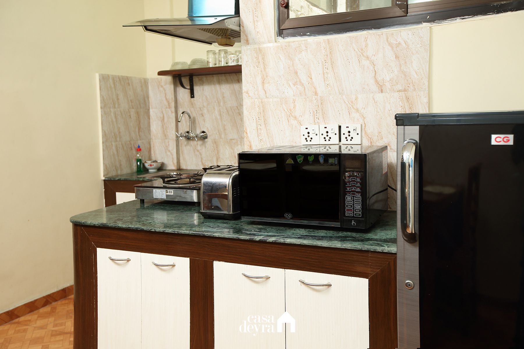 A kitchen with a microwave, toaster, and refrigerator on a marble countertop.