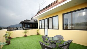 A rooftop terrace with artificial grass, potted plants, and wicker furniture.