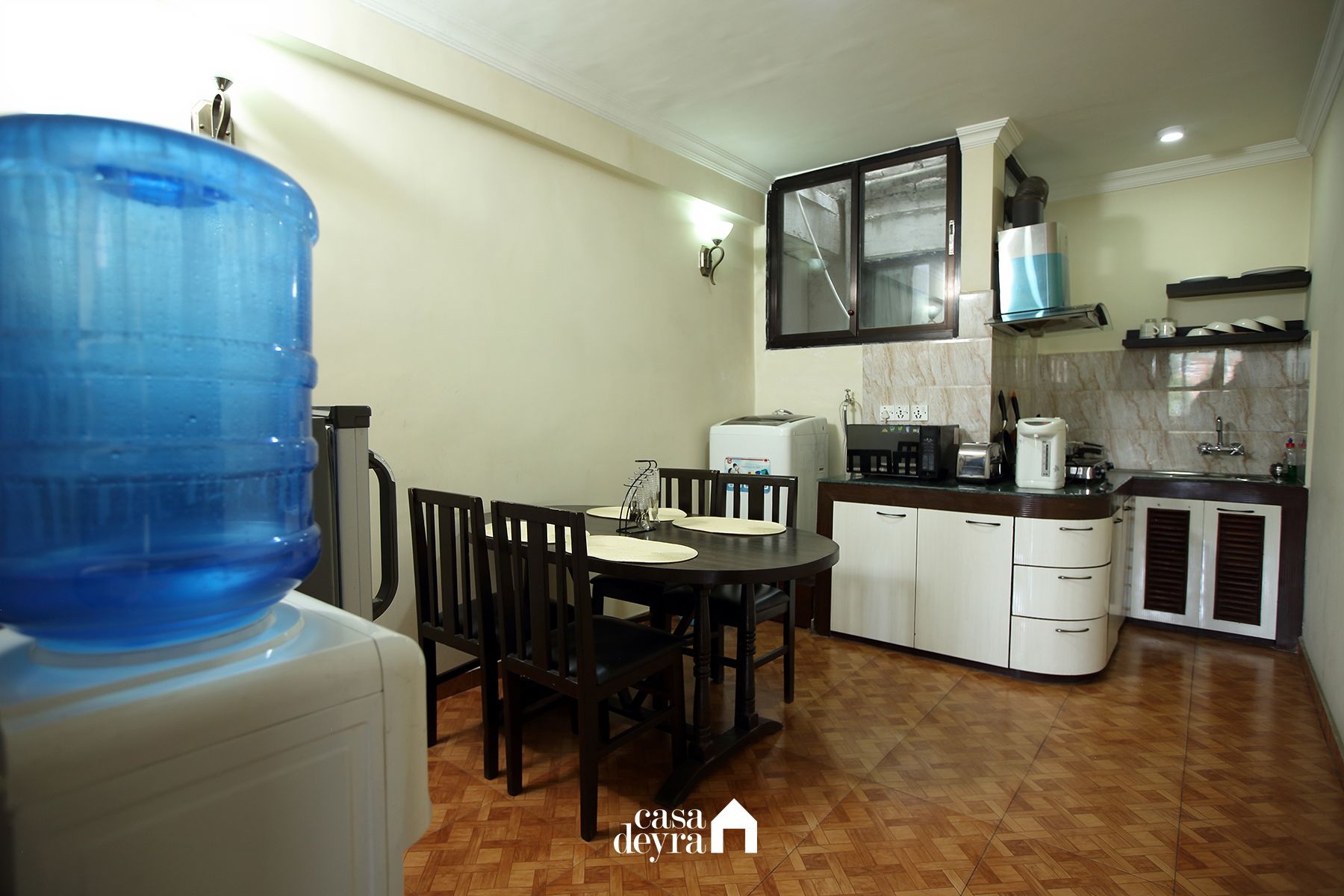 Cocina compacta con comedor, dispensador de agua, refrigerador, microondas, tostadora y lavabo.