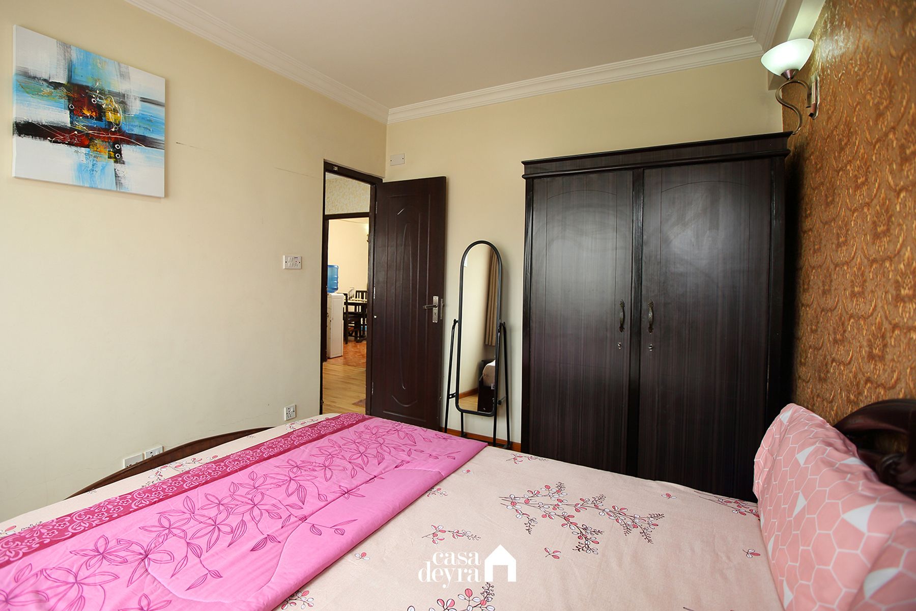 A bedroom with a bed, a wardrobe, a mirror, and a painting on the wall.