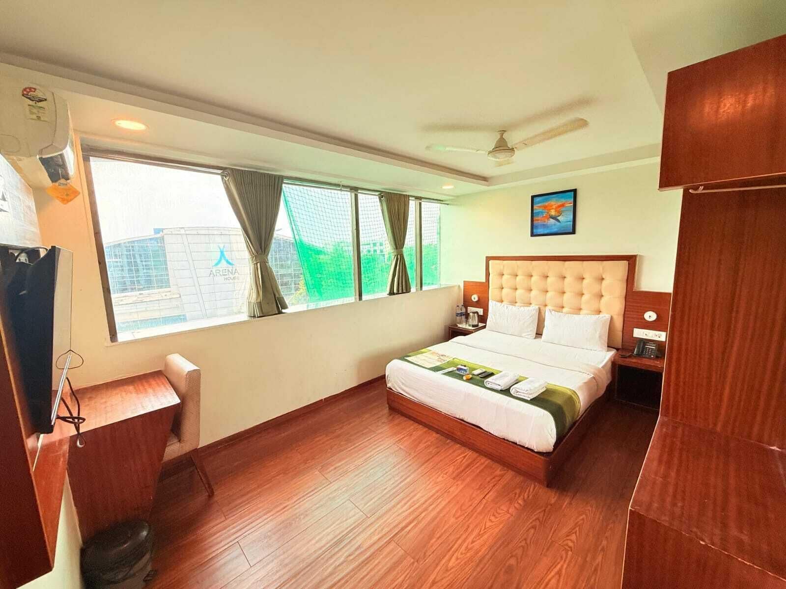 A hotel room with a bed, a desk, a chair, a ceiling fan, and a window with curtains.