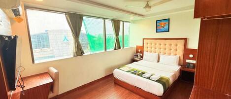 A hotel room with a bed, a desk, a chair, a ceiling fan, and a window with curtains.