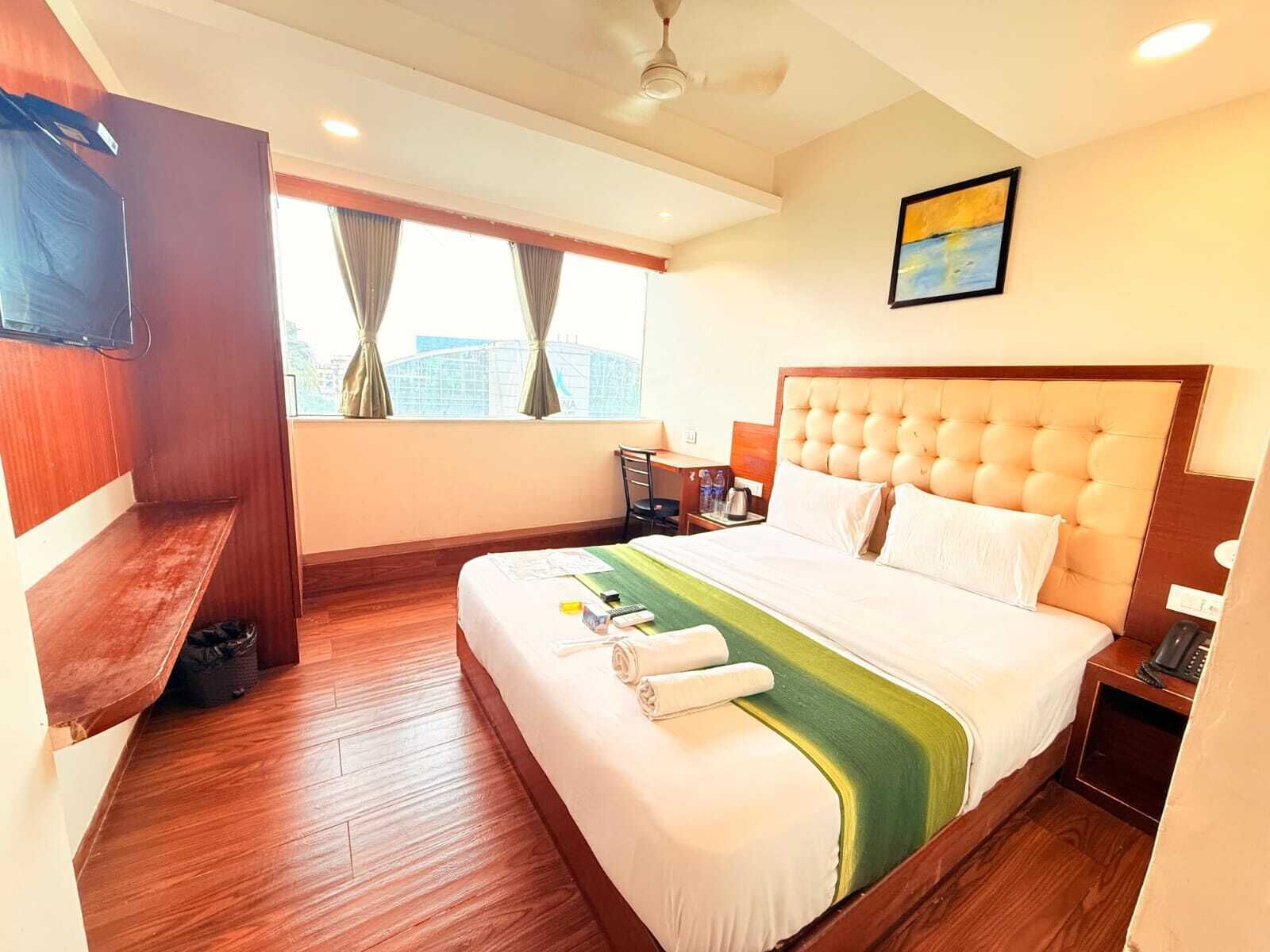 A hotel room with a large bed, a desk, a chair, a TV, and a window with curtains.