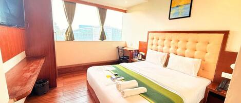 A hotel room with a large bed, a desk, a chair, a TV, and a window with curtains.
