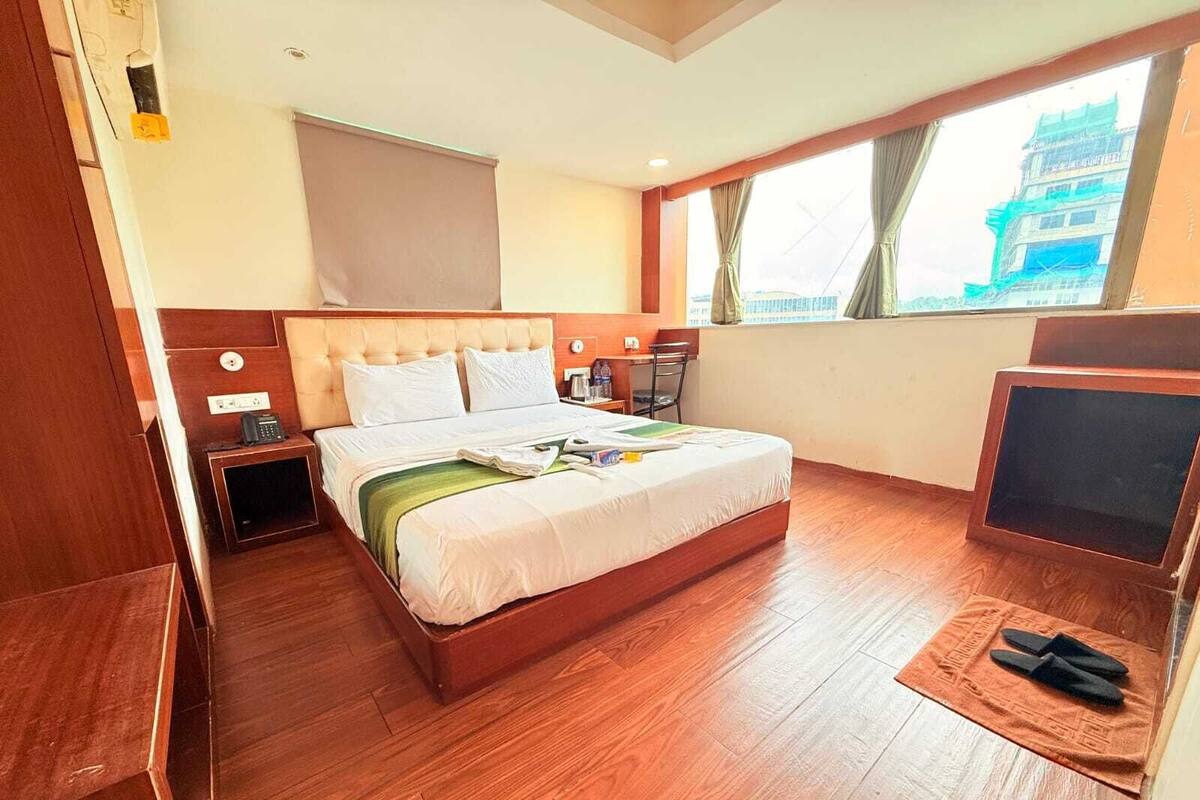 A hotel room with a bed, a desk, a chair, a TV, and a window with curtains.