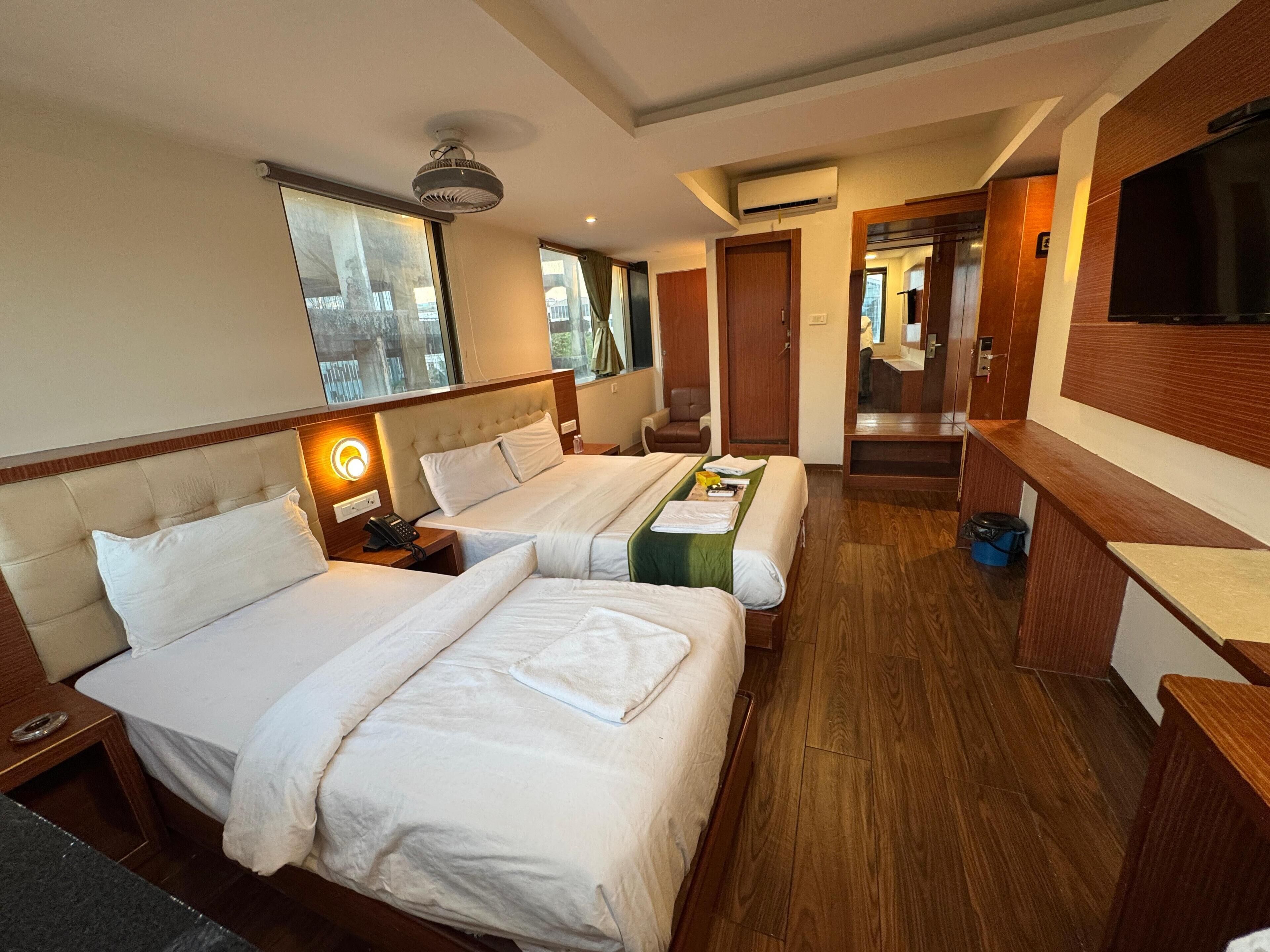 A hotel room with two beds, a desk, a chair, a TV, and a bathroom visible through an open door.