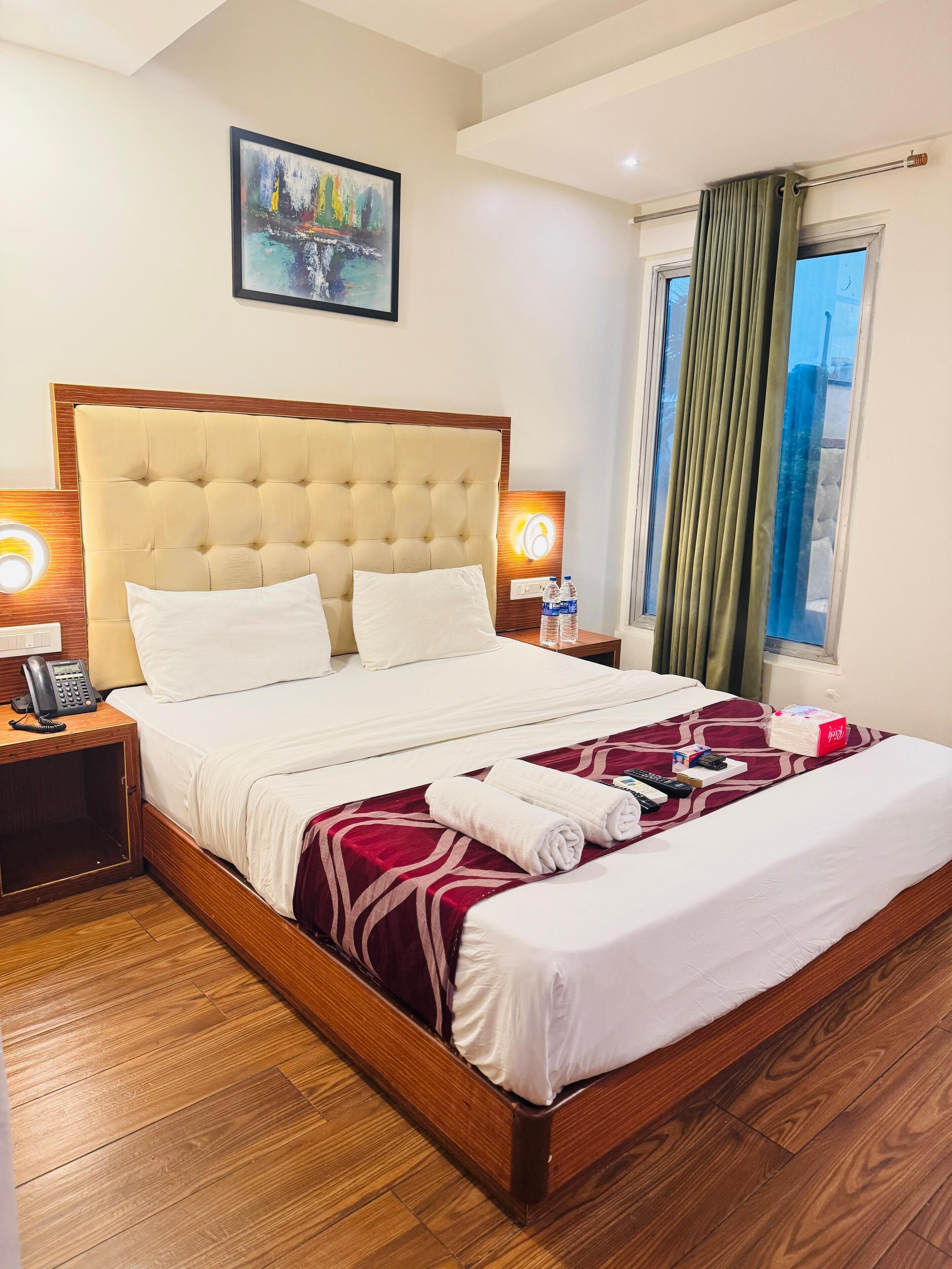 A hotel room with a large bed, wooden headboard, bedside lamps, a painting on the wall, and a window with curtains.