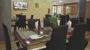 A dining area with a wooden table, black chairs, and a TV mounted on the wall. - Gold Crown Hotel (Owerri)