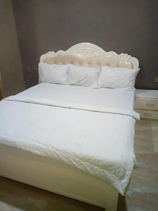 A bed with a white headboard and pillows, a white bedspread, and a tiled floor.