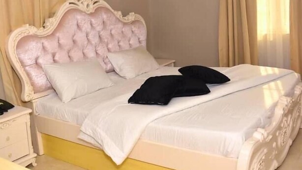 A bedroom with a bed, a nightstand, and an air conditioning unit on the wall. - Gold Crown Hotel (Owerri)